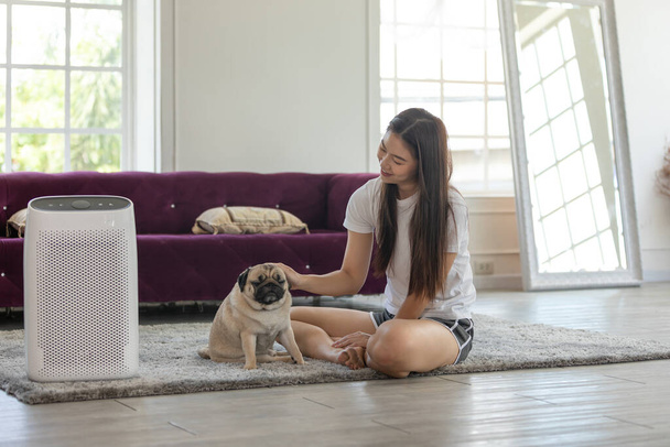Woman playing with Dog Pug Breed and Air purifier in cozy white bed room for filter and cleaning removing dust PM2.5 HEPA in home,for fresh air and healthy life,Air Pollution Concept - Photo, Image
