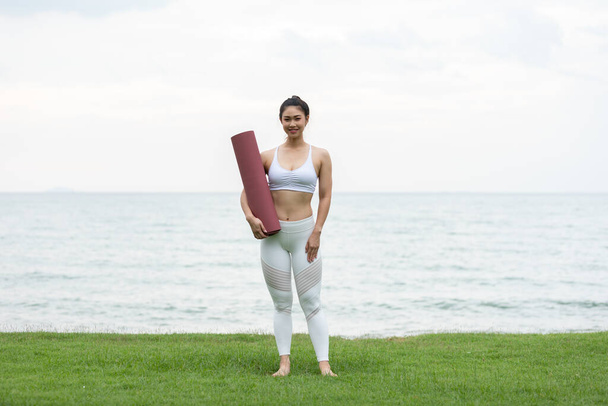 Asian young woman holding yoga mat and smile on the beach,ready to practice yoga with happiness feeling - Photo, image