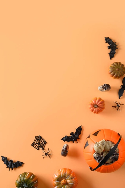Halloween party decorations, candy bowl, pumpkins, sweets, bat, skulls, spooky spider on orange background. View from above, flat lay. Vertical format for invitation. - 写真・画像