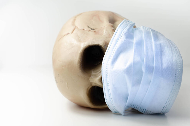 Ijesztő emberi koponya orvosi maszkot visel, szimbolikus ábrázolása halál vírusos járvány, coronavirus - Fotó, kép