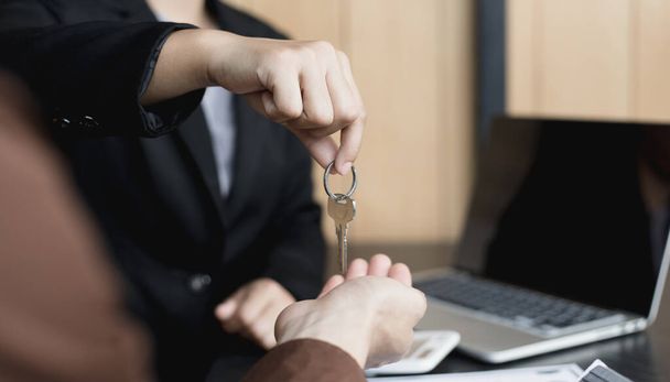 Verkaufsleiter oder Immobilienmakler hält den Schlüssel in der Hand und übergibt ihn dem Kunden nach Unterzeichnung des Hauskaufvertrages mit der Hausversicherung, dem Handel mit Hypotheken und dem Versicherungskonzept. - Foto, Bild