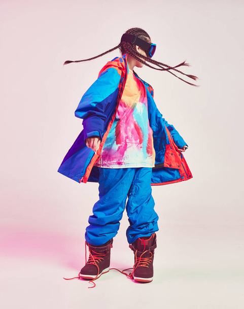 Cool sporty young female in stylish colorful winter sportswear with pigtails shakes head in studio in neon light - Φωτογραφία, εικόνα