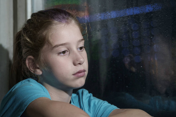 Brązowe oczy dziewczyny w niebieskiej koszuli na parapecie na zamglone okno z zamglonym tle nocy - Zdjęcie, obraz