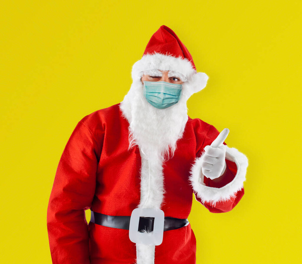 Санта-Клаус Санта-Клаус в хирургической маске показывает большой палец вверх показывает большой палец вверх на желтом фоне. - Фото, изображение