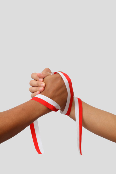 Las manos de un hombre sosteniendo una cinta roja y blanca como símbolo de la bandera indonesia. Aislado sobre fondo gris - Foto, Imagen