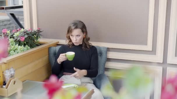 Μια νεαρή γυναίκα με ένα φλιτζάνι καφέ ή τσάι έχει μια συναισθηματική συνομιλία. Χειρονομίες κατά τη διάρκεια μιας συζήτησης. - Πλάνα, βίντεο