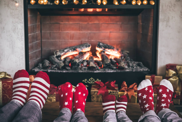 Happy family with children near fireplace at Christmas. Feet wearing Xmas socks. Winter holiday concept - Foto, imagen