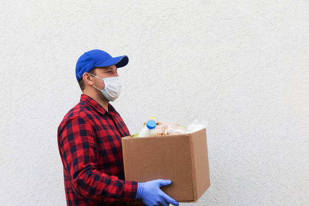 el voluntario en una máscara protectora con una caja de comida, donación - Foto, imagen