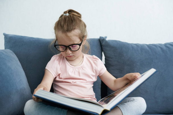 Ein kleines Mädchen liest Buch mit Brille. Ein lächelndes kleines Mädchen hält ein Buch in der Hand. Ein kleines Mädchen liest und lächelt - Foto, Bild