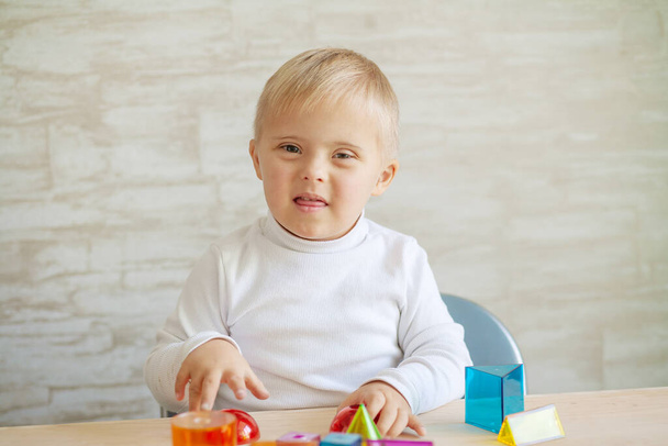 Des petits garçons mignons avec une maladie génétique sont assis à la table. enfant avec trisomie 21 joue avec des figures géométriques 3D. Plastique dans les jouets. - Photo, image