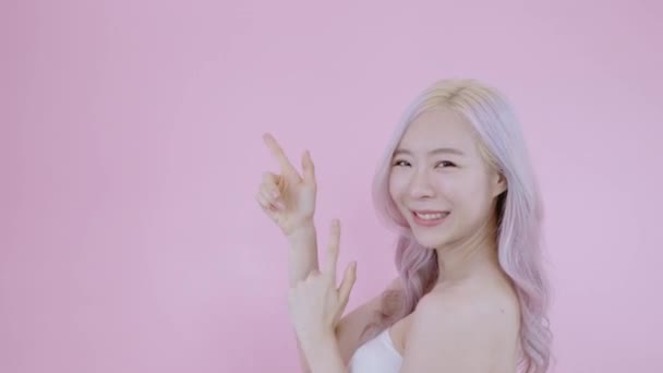 アジアの女性は向きを変え、顧客のための指ポイントコピースペースは旗プロダクト広告を適用する。現代のブロンズとピンクの髪美しいです女性モデルオン隔離ピンクバックグランド着用セクシーホワイトブラジャー - 映像、動画