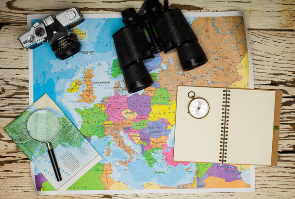 Flat lay of the travel planning concept. Top view of a diary, binoculars, compass, retro photo camera, and Europe map on a white wooden table - Photo, Image