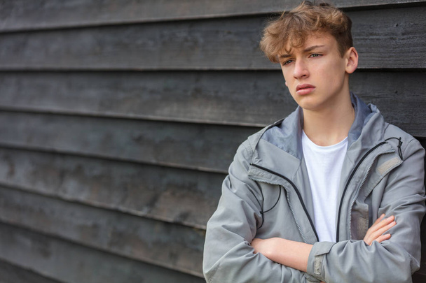 Serious male boy teenager outside leaning against a wall wearing looking sad, moody, thoughtful or depressed - Fotoğraf, Görsel
