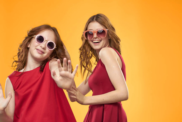 黄色の背景に赤いドレスの幸せな姉妹は楽しさとジェスチャーを持っていますコピースペース - 写真・画像