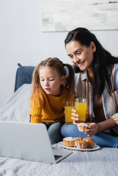 mother and daughter with muffins and orange juice watching film on laptop - 写真・画像