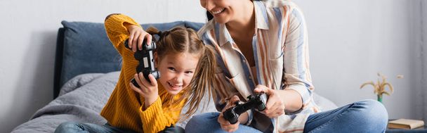 KYIV, UKRAINE - SEPTEMBER 15, 2020: excited woman and child playing video game in bedroom, banner - Photo, image