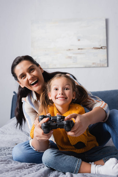 KYIV, UCRAINA - 15 SETTEMBRE 2020: madre e figlia eccitate che giocano ai videogiochi in camera da letto - Foto, immagini