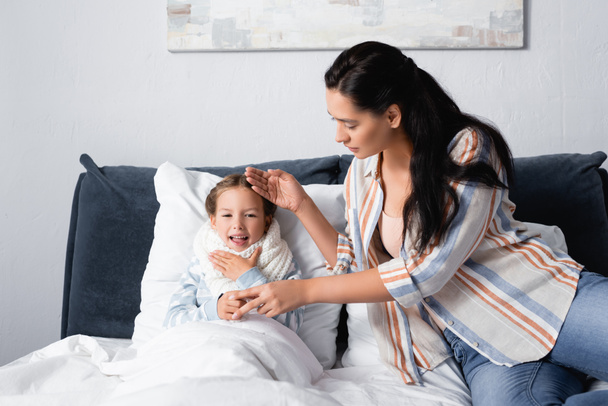 madre tocando la frente de la enferma, tosiendo hija acostada en la cama - Foto, imagen
