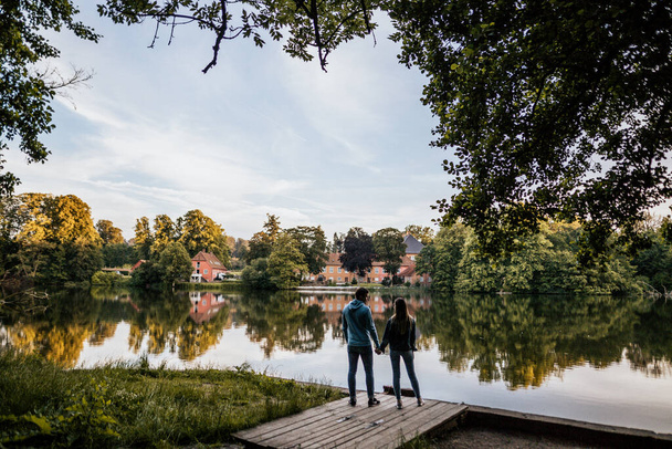 Горизонтальна фотографія романтичної пари стоїть біля озера і тримає руки на фоні природи. Щасливий чоловік і жінка в джинсовому одязі
 - Фото, зображення
