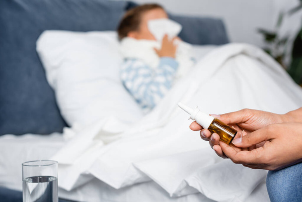 woman holding nasal spray near sick daughter lying in bed on blurred background - Fotoğraf, Görsel