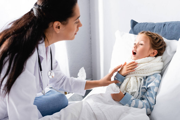 pediatrician examining sore throat of diseased girl lying in bed - Fotoğraf, Görsel