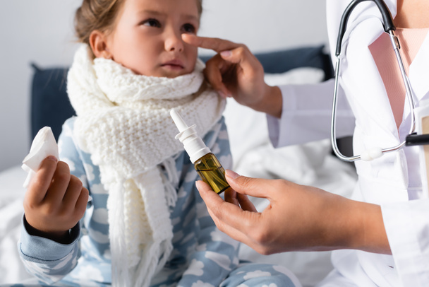 doctor pointing at nose of diseased girl while holding nasal spray on blurred background - Zdjęcie, obraz