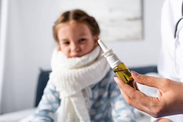 doctor holding nasal spray near sick girl on blurred background - Foto, afbeelding