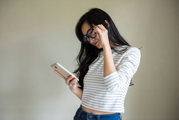 Satisfied lovely woman with glasses hold modern cell phone, texts with friend online in chat, dressed in stylish clothes, connected to high speed internet. Asian teenager with smartphone device. - Photo, Image