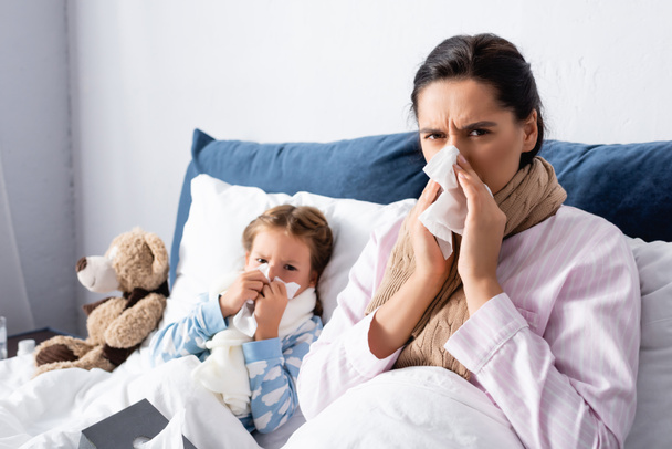 madre enferma y el niño estornudando en servilletas de papel mientras mira a la cámara - Foto, Imagen