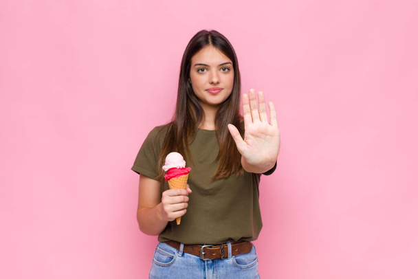young pretty woman with an ice cream looking serious, stern, displeased and angry showing open palm making stop gesture - Zdjęcie, obraz
