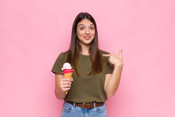 young pretty woman with an ice cream feeling happy, surprised and proud, pointing to self with an excited, amazed look - Foto, immagini