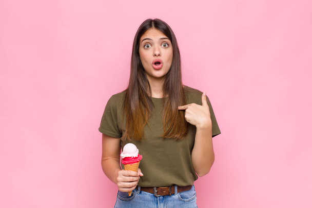 young pretty woman with an ice cream looking shocked and surprised with mouth wide open, pointing to self - Foto, afbeelding