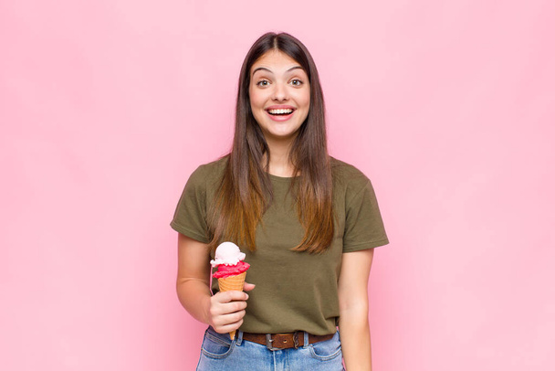 young pretty woman with an ice cream looking happy and pleasantly surprised, excited with a fascinated and shocked expression - Φωτογραφία, εικόνα