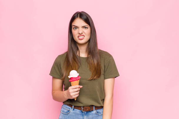 young pretty woman with an ice cream feeling puzzled and confused, with a dumb, stunned expression looking at something unexpected - Foto, Bild