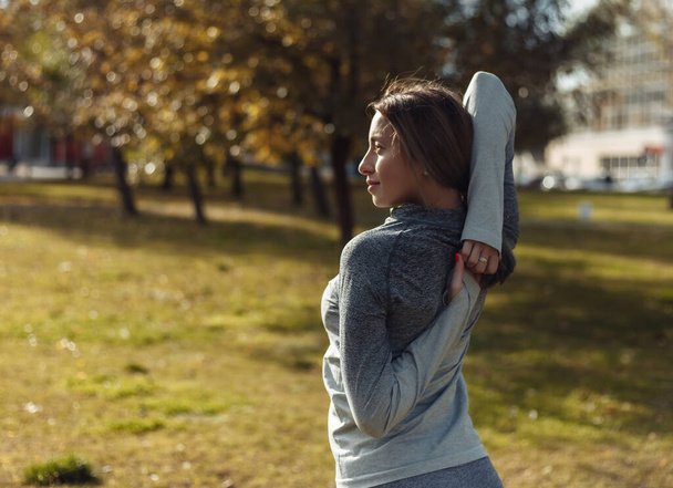 Молода спортивна жінка в спортивному костюмі розігрівається в осінньому парку. Розтягування рук перед тренуванням. Фітнес тренування на відкритому повітрі
 - Фото, зображення