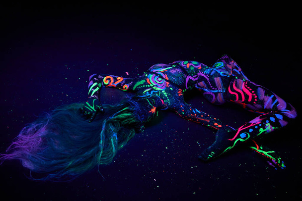 Art woman body art on the body dancing in ultraviolet light. Bright abstract drawings on the woman body neon color. Colored hair and face - 写真・画像