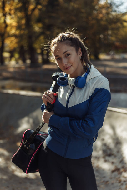 Spor kıyafetli, çantalı ve kulaklıklı genç bir kadın spor parkında yürüyor.. - Fotoğraf, Görsel
