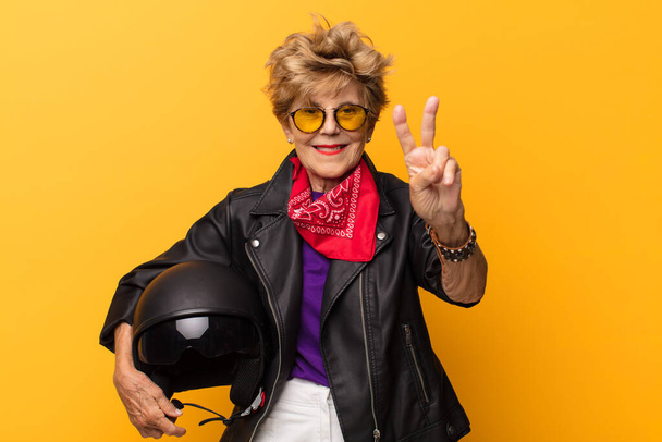 mature old beautiful woman smiling and looking happy, carefree and positive, gesturing victory or peace with one hand. motorbike concept - Foto, afbeelding