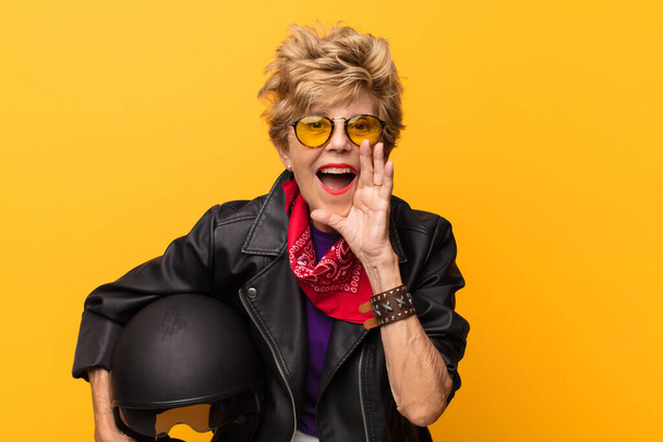 mature old beautiful woman feeling happy, excited and positive, giving a big shout out with hands next to mouth, calling out. motorbike concept - Photo, Image