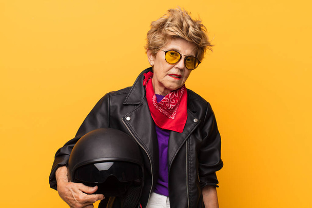 mature old beautiful woman feeling puzzled and confused, with a dumb, stunned expression looking at something unexpected. motorbike concept - Foto, imagen