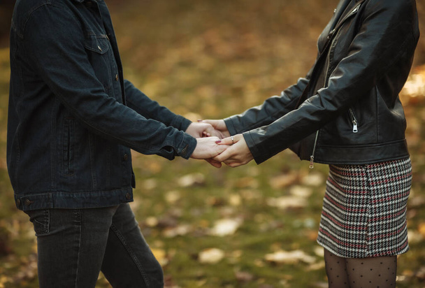 Romantic, love concept. Young couple in love holds hands on a blurry background of fallen autumn leaves in the park. Romantic date - Photo, Image