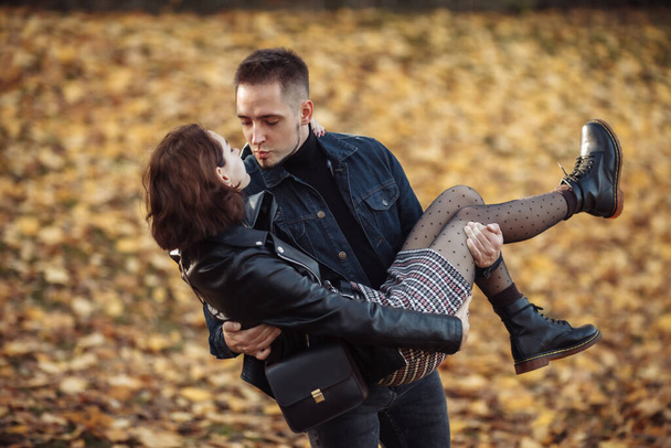 Romantic, love concept. A bearded man holds in his arms a young attractive woman in autumn park. Young couple in love spend time together outdoors - Photo, Image