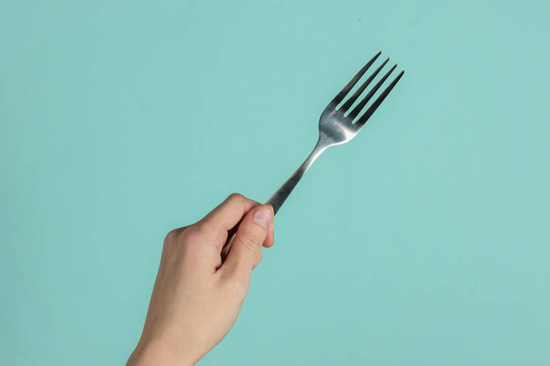 Female hand holds a fork on blue pastel background. Top view. Studio shot - Foto, afbeelding