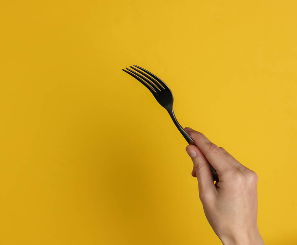 Female hand holds a fork on a yellow background. Top view. Studio shot - Foto, imagen