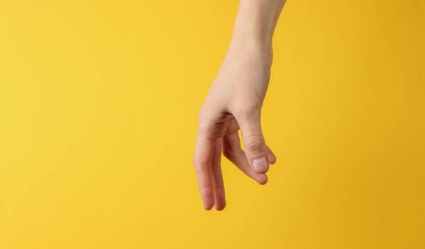Female hand reaches out to take on yellow background. - Fotografie, Obrázek