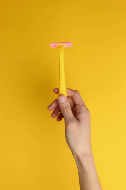 Female hand holds yellow disposable razors of epilators on yellow background. Beauty and fashion shot - Foto, afbeelding