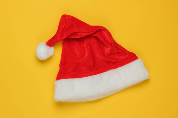 Sarı arka planda Noel Baba şapkası. Yeni yıl, Noel minimalist konsepti. Üst manzara, stüdyo çekimi.. - Fotoğraf, Görsel