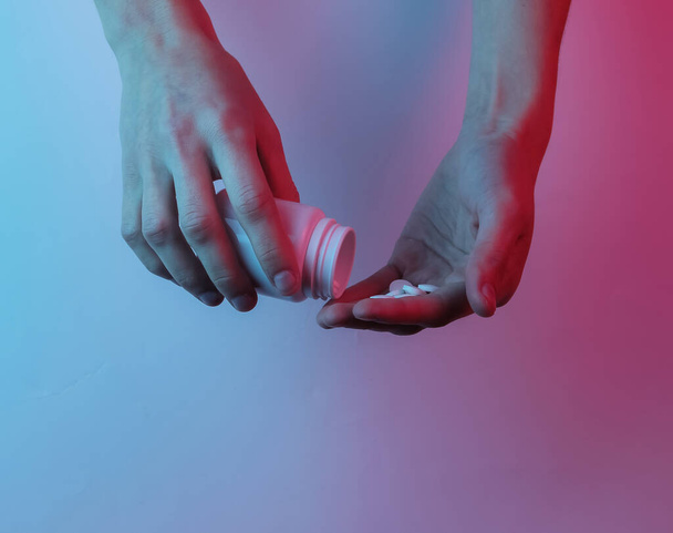 Drugs. Hand holds a bottle of pills and tablets. Creative pop art pink blue neon color. Trendy gradient illumination. Night light - Foto, afbeelding