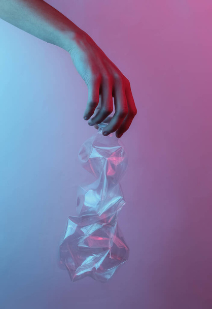 Újrahasznosítási koncepció. A női kéz egy összetört műanyag palackot tart. Creative pop art rózsaszín kék neon szín. Trendi gradiens megvilágítás. Éjszakai fény - Fotó, kép