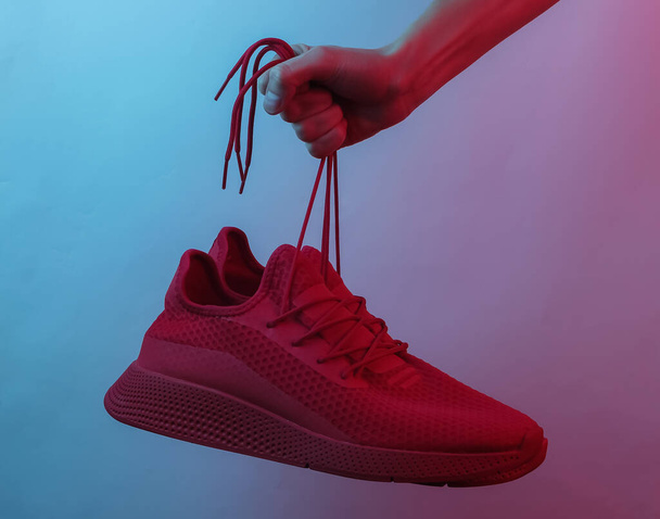 Kadın eli kırmızı spor ayakkabılarını bağcıklarından tutar. Yaratıcı pop sanatının pembe neon rengi. Moda eğilimli aydınlatma. Gece lambası - Fotoğraf, Görsel